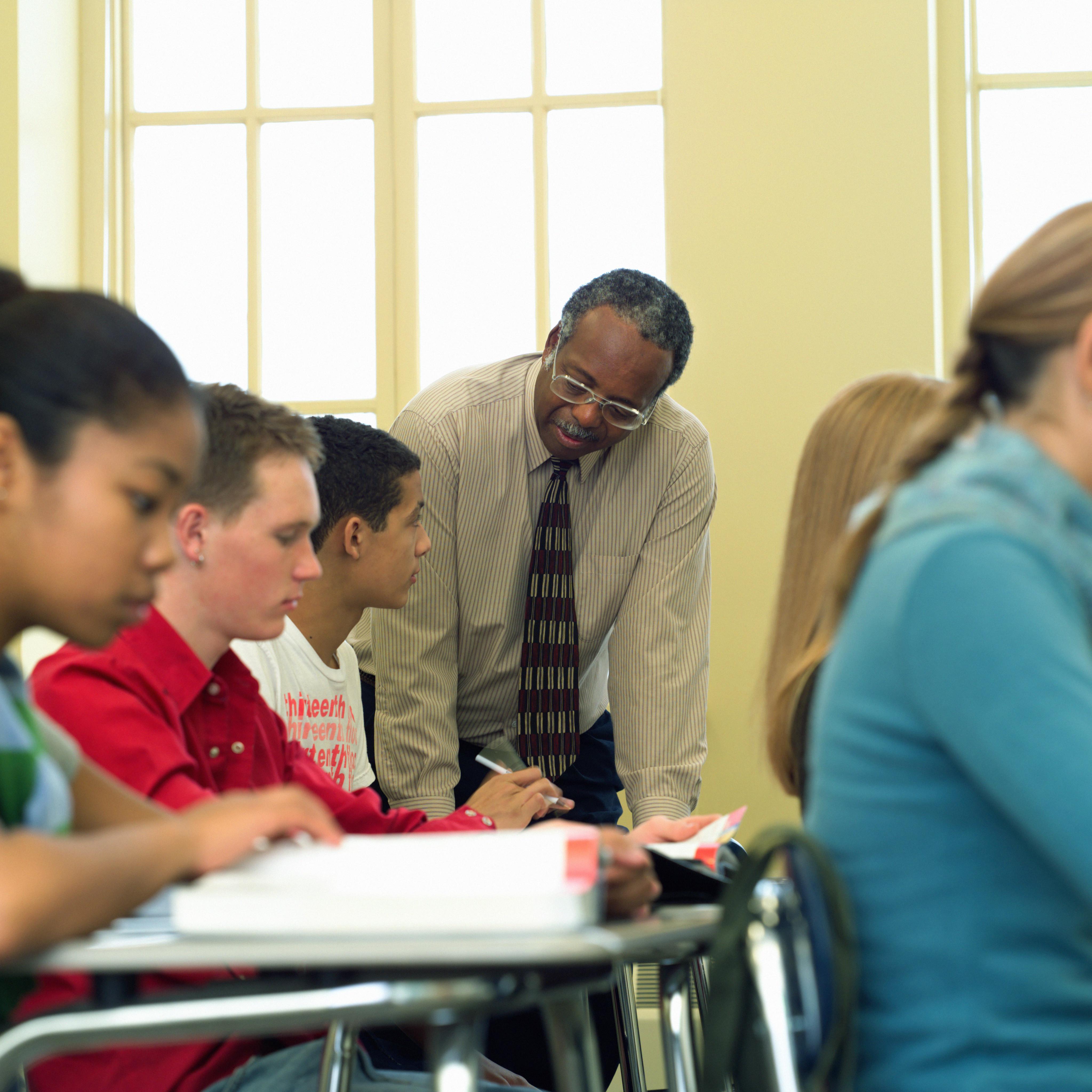 Teacher leaning over students desk, high school classroom