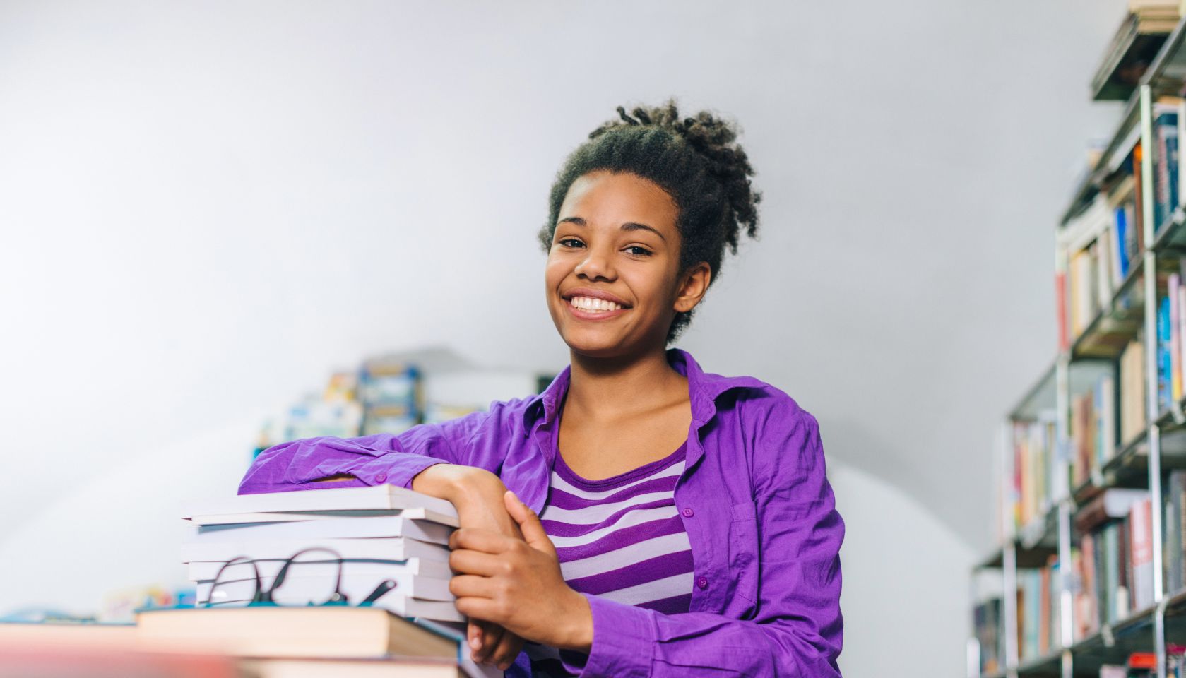 Pensive black girl in library posing with books