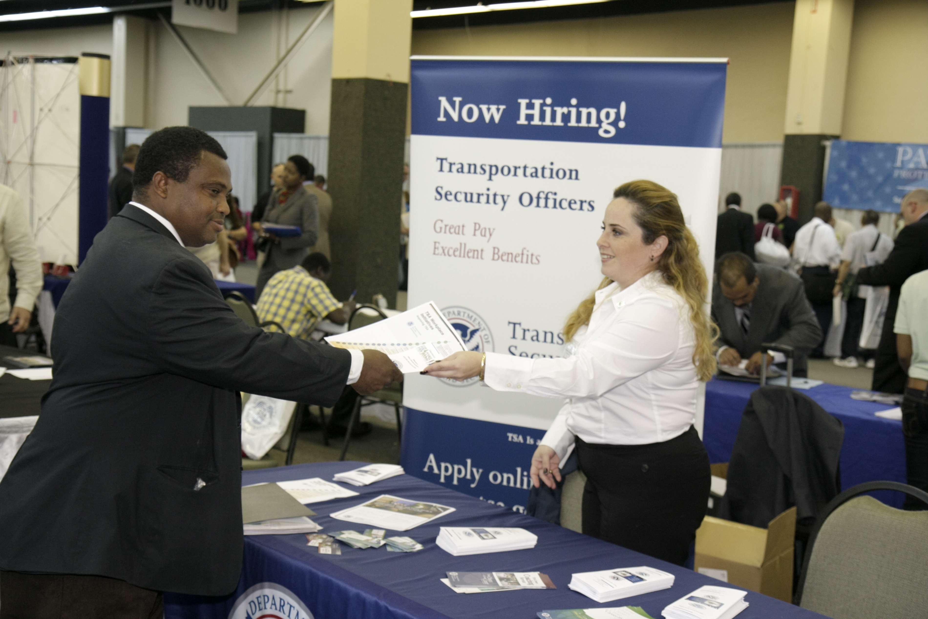A woman handing a brochure to a man at the Transportation Security Administration booth at a job fair in Miami
