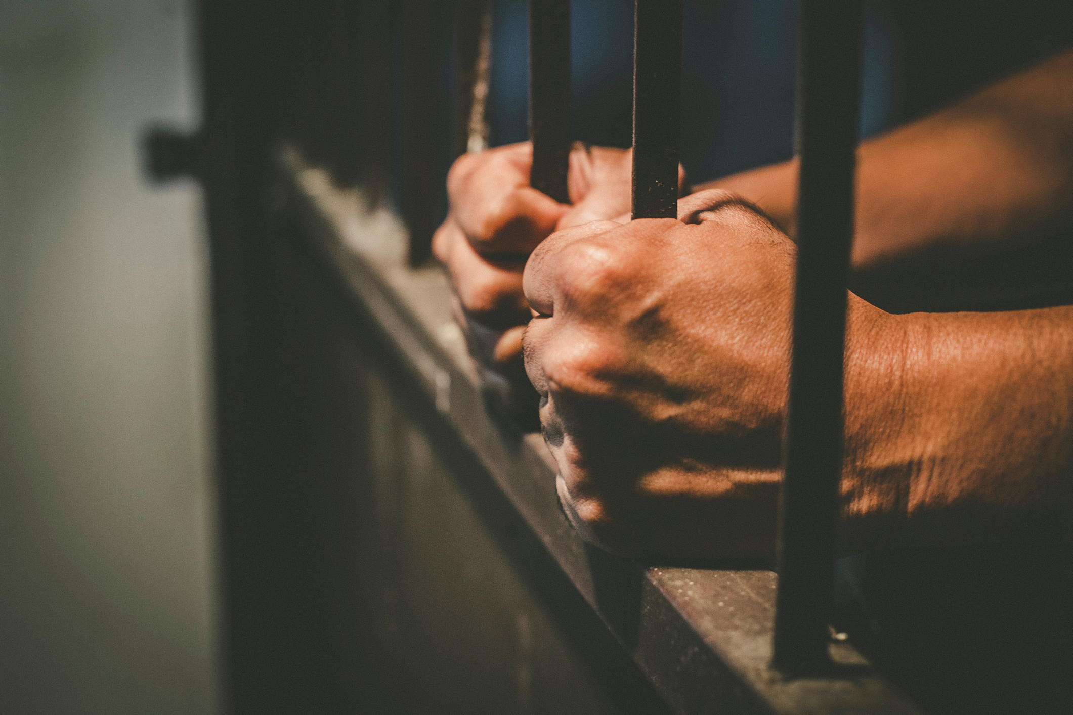 Cropped Hands Of Male Prisoner Holding Prison Bars