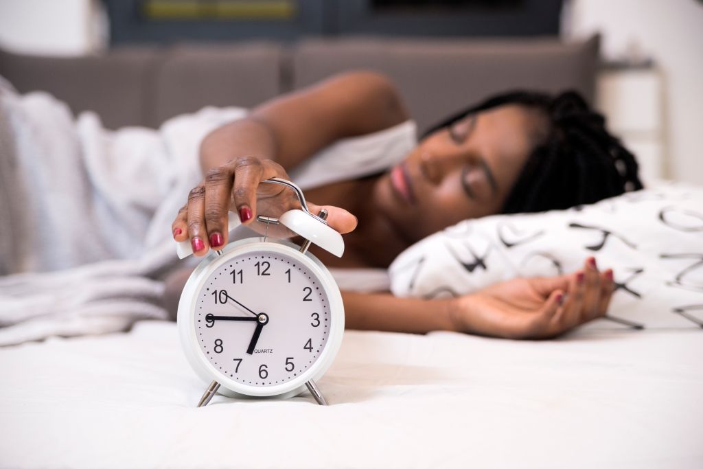 Tired woman switching off her alarm clock in her bedroom. Sleepmaxxing