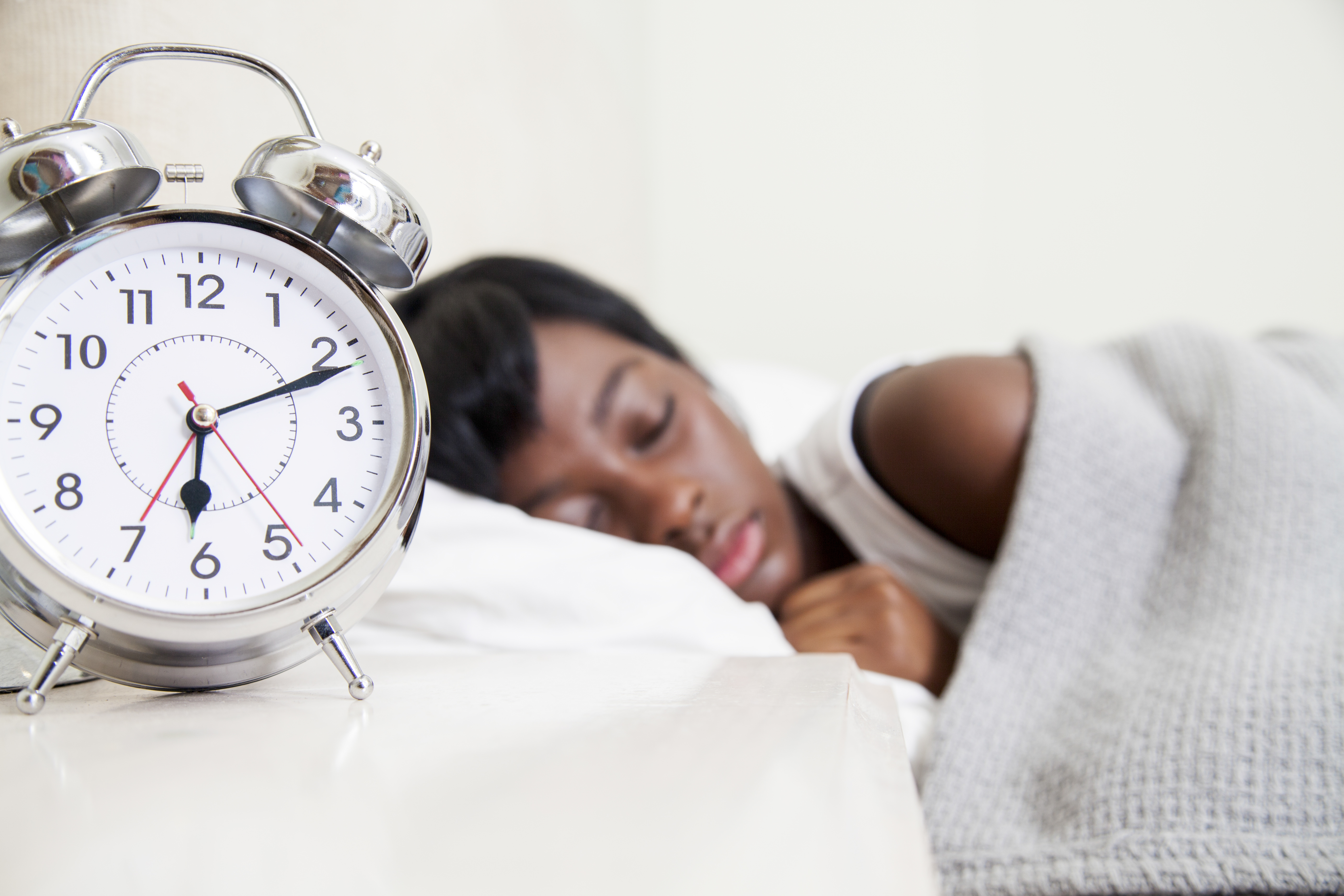 African teenaged girl sleeping, double bell alarm clock foregrounded, Cape Town, South Africa