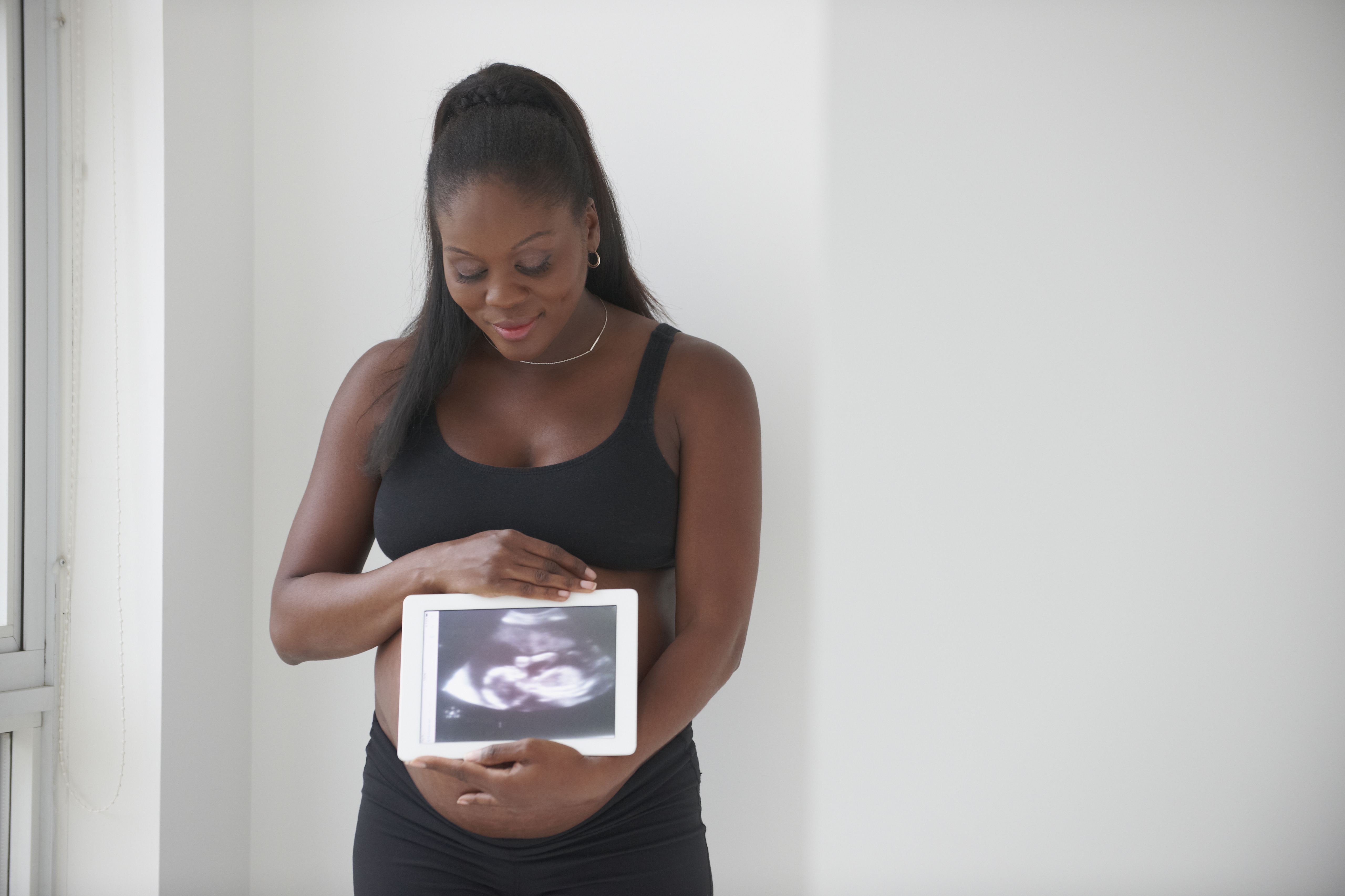 Pregnant Black woman showing sonogram on digital tablet
