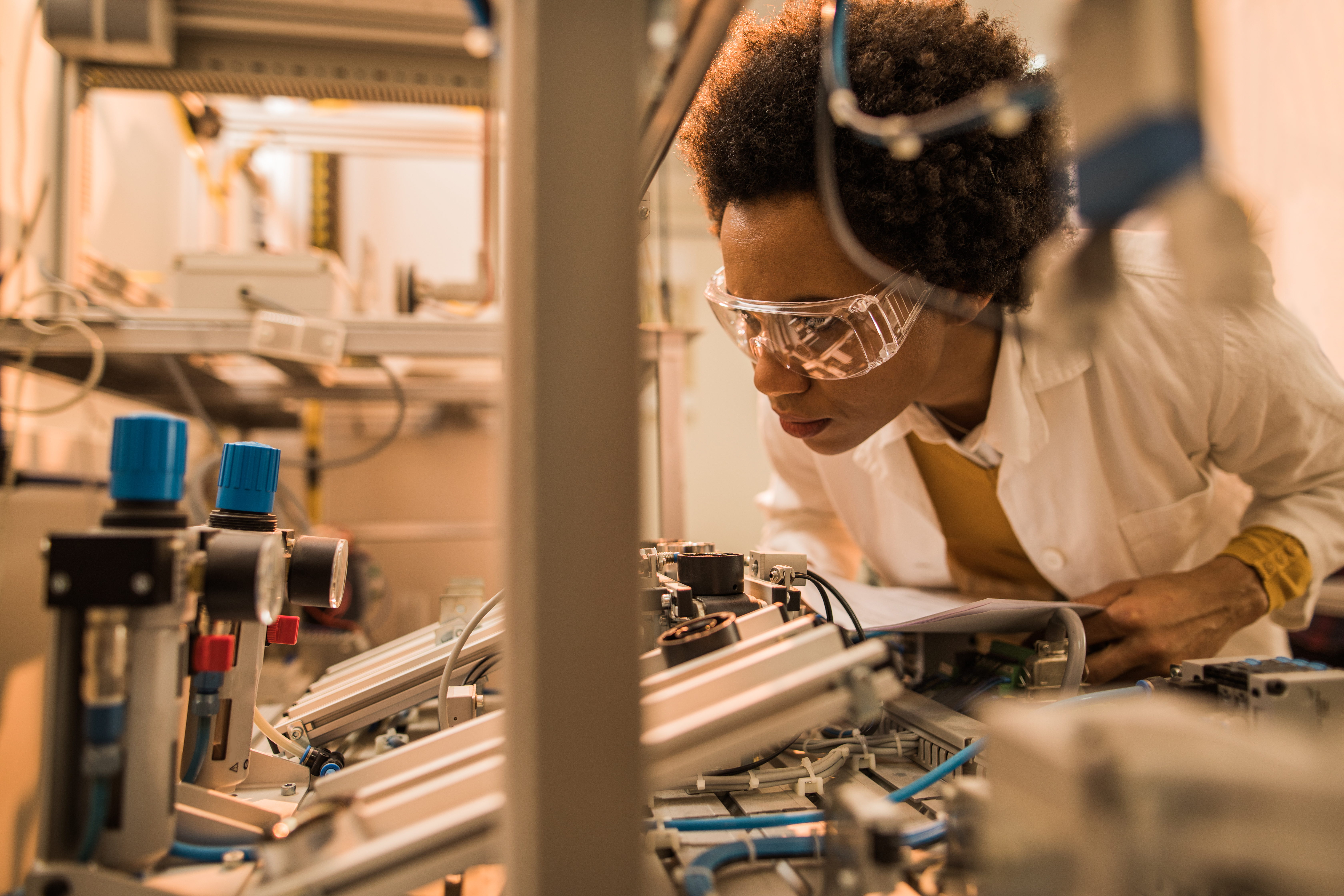 African American quality control inspector examining machine part on production line.