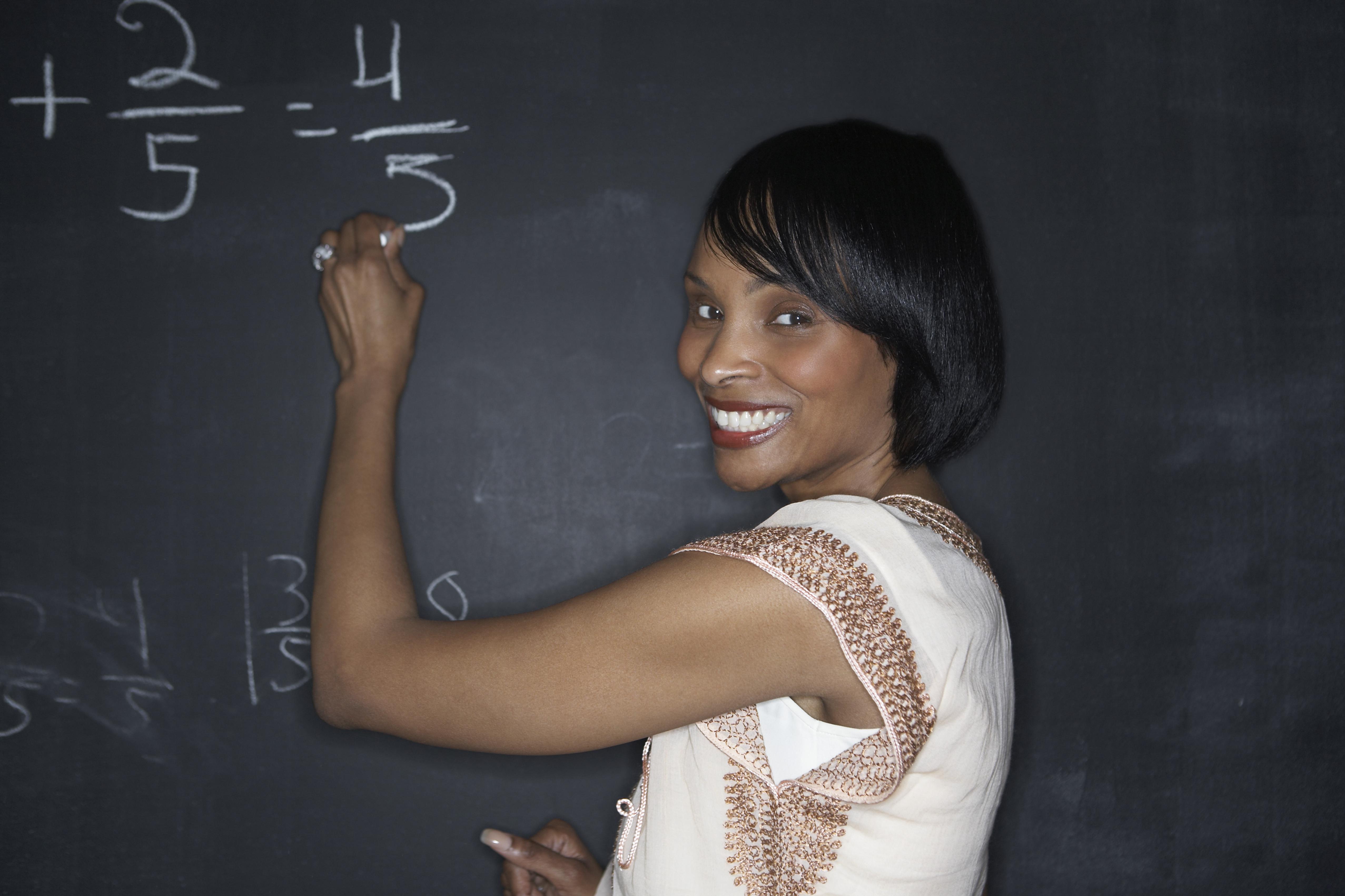 Teacher writing with chalk on a blackboard.