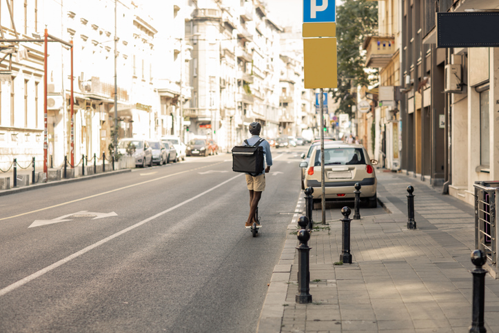 Young African Delivery Man Riding Electric Scooter In the City