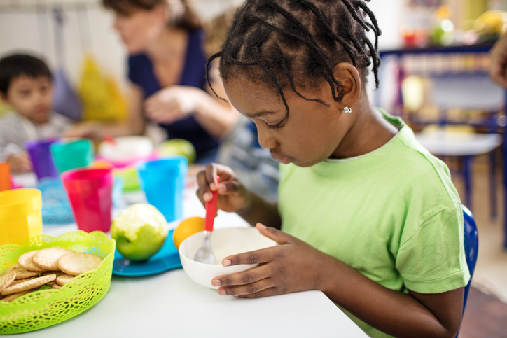 Cute girl eating from bowl by in preschool