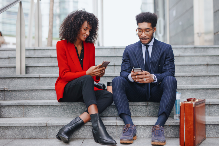 Young business couple using smart phone while sitting on the staircase in downtown district