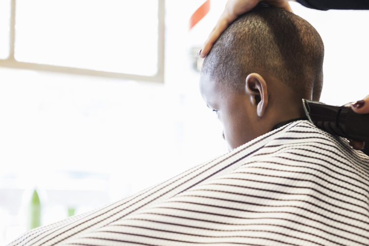 Hairdresser clipping hair of boy in retro barbershop