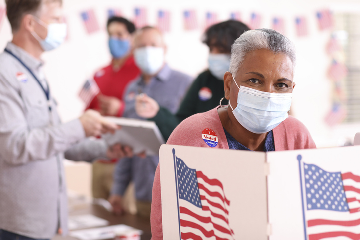 Senior adult, African descent woman votes in USA election wearing mask.