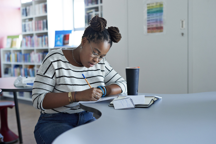 Confident female student writing on paper at desk