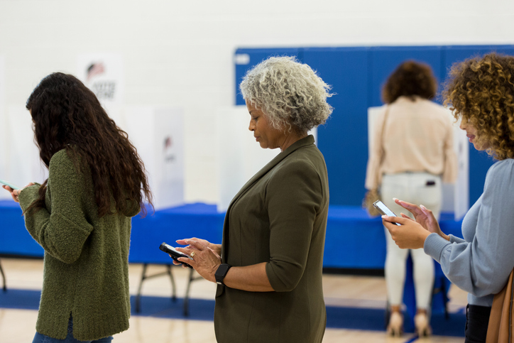 Women of varying ages standing in line use smart phones