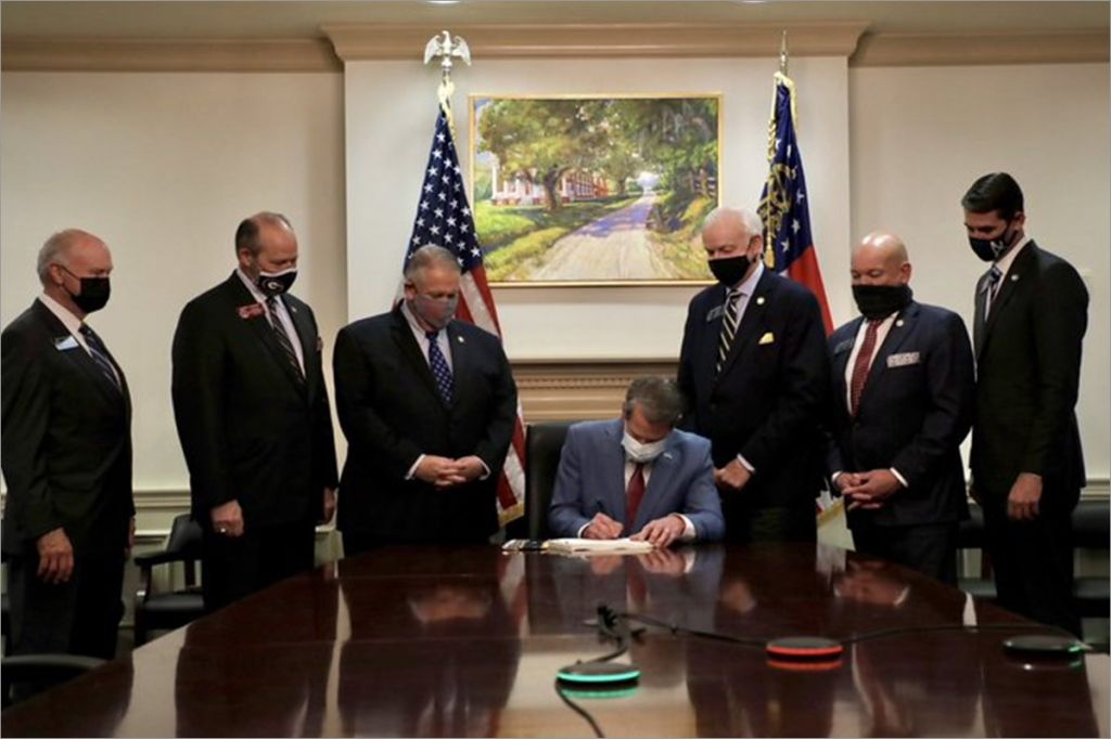 Georgia Gov. Brian Kemp signs voter suppression laws in front of painting of slavery plantation