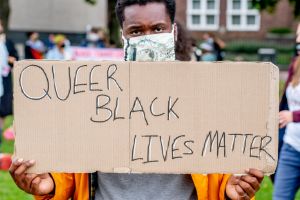 A protester holds a placard that says Queer Black Lives...