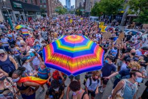 A participant holding a rainbow umbrella over the crowd of...