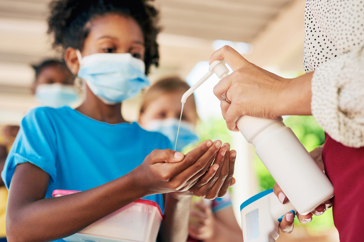 Shot of a young girl wearing a face mask and sanitising her hands during recess at school