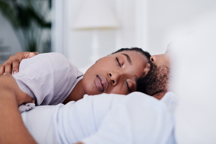 Shot of a young couple cuddling while sleeping in bed together at home