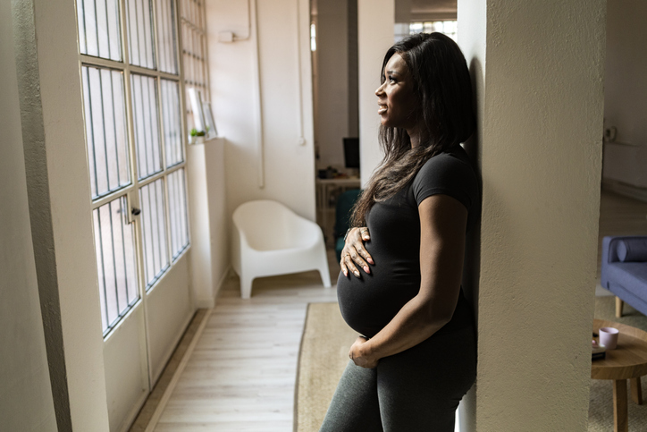 Thoughtful young pregnant woman leaning against column at home