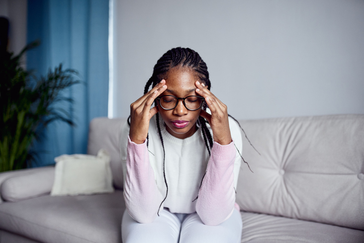 A young girl is sitting on the couch at home with her head in her hands. anxiety