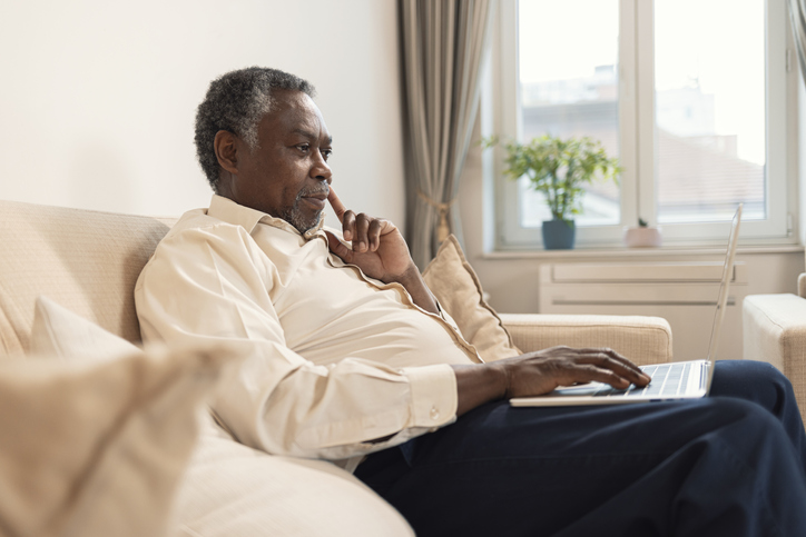 Senior Man Sitting On Sofa Using Laptop At Home