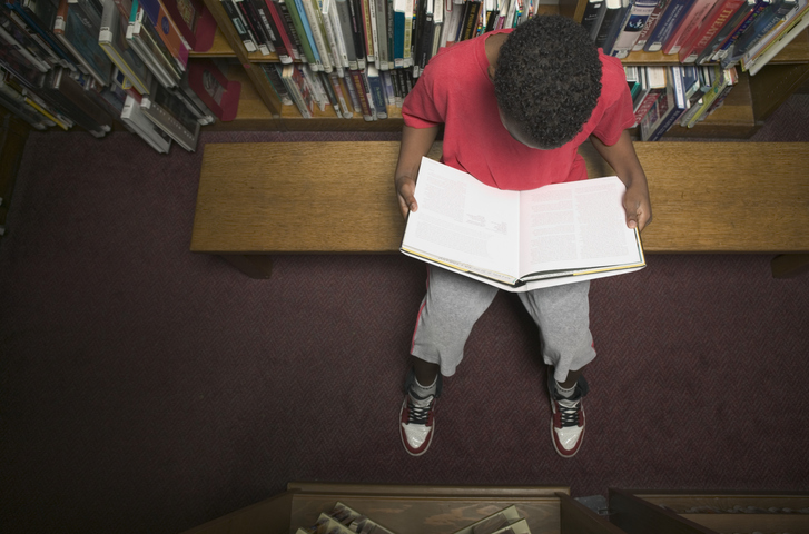 High angle view of a young boy reading a book in a library
