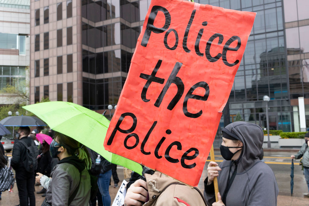 Black Lives Matter activist holds sign reading "police the...