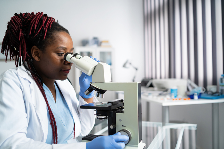African-american scientist woman or graduate student in a lab coat and protective face mask works in modern laboratory