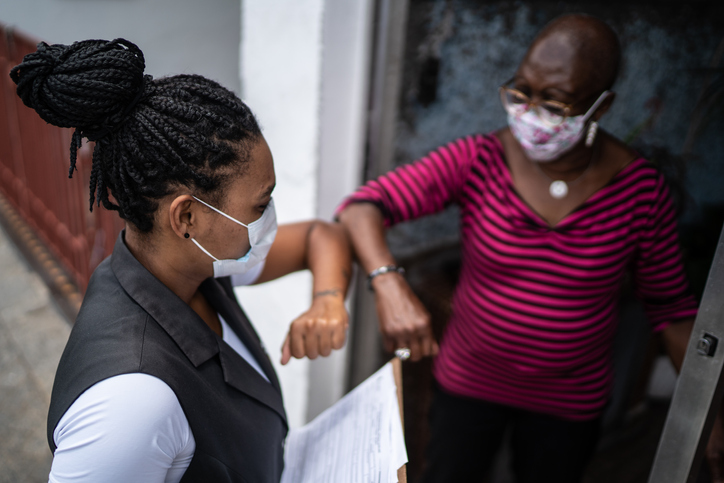 Surveyor greeting senior woman in the doorway - wearing face mask