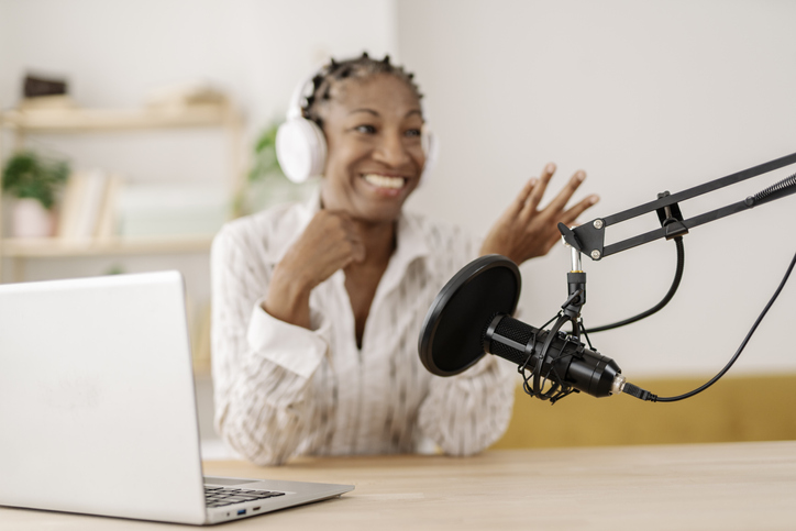 Smiling freelancer recording podcast through microphone at home office