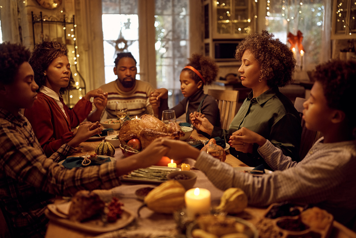 African American extended family saying grace while having Thanksgiving meal at dining table.