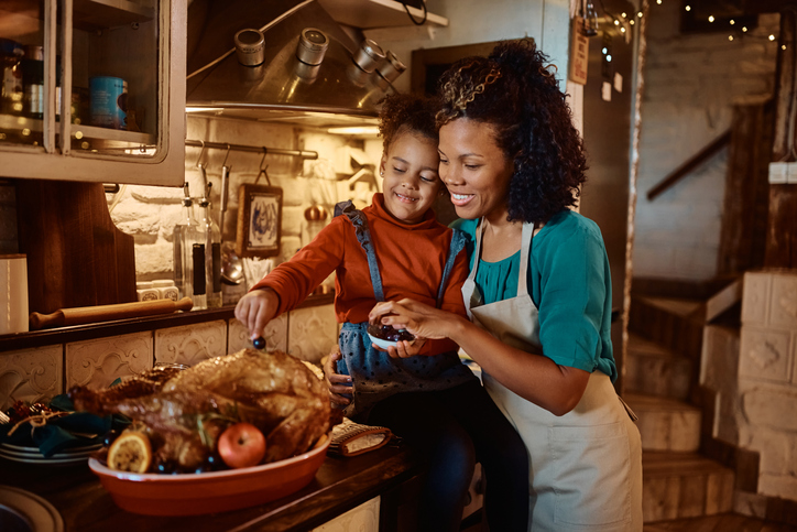 Happy black mother and her small daughter decorating roast turkey for Thanksgiving lunch.