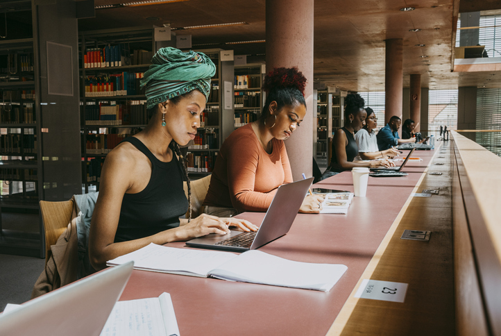 Woman wearing turban using laptop while sitting with friend in library