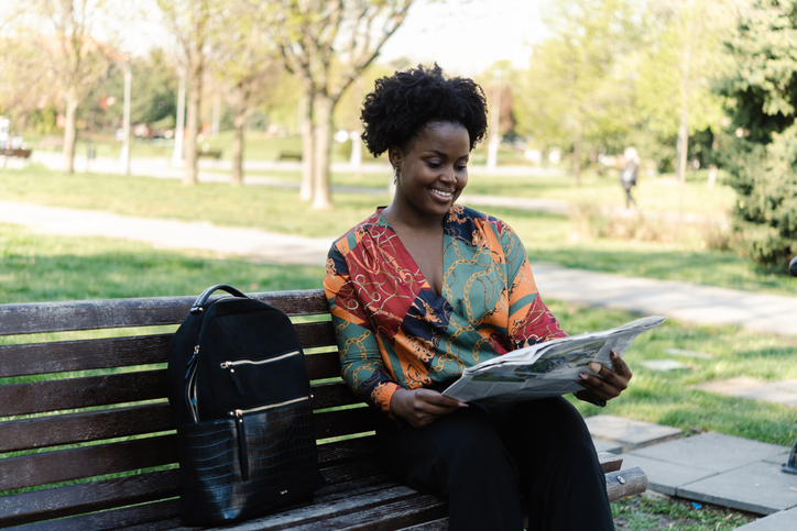 Portrait of a young woman sitting at the park and reading newspaper