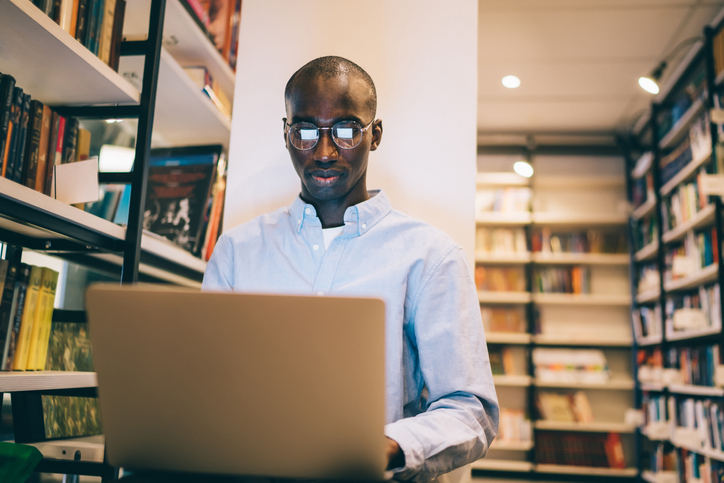 Black man in glasses using laptop in library