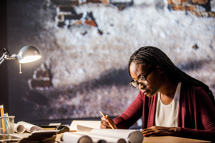 Diligent female architect drawing blueprints for a project late at night
