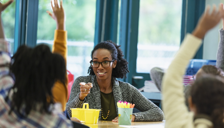 Teacher in classroom points to student raising hand