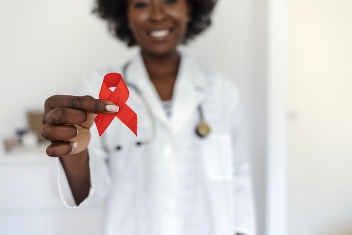 Woman doctor with stethoscope showing pink ribbon, breast cancer awareness.