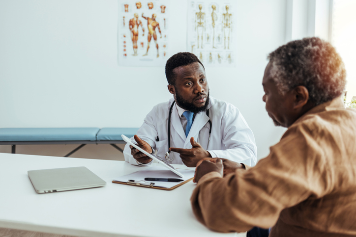 Friendly and Cheerful Family Doctor is Reading Medical History of Senior Male Patient During Consultation