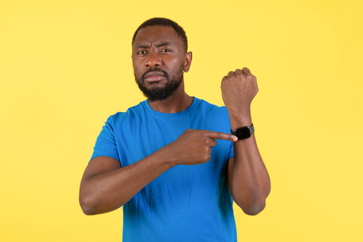 Discontented African American Man Showing Smartwatch Over Yellow Background
