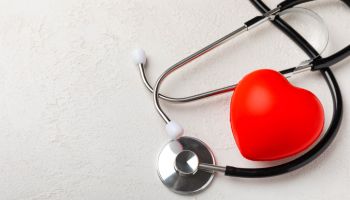 Black stethoscope and red heart, on a white textural background, close-up. Healthcare. Place for text. Medicine concept. The concept of cardiology.
