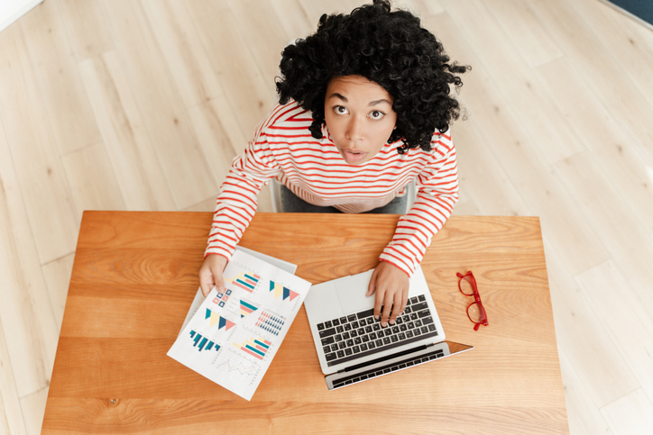Portrait of excited African American businesswoman sitting at desk, using laptop