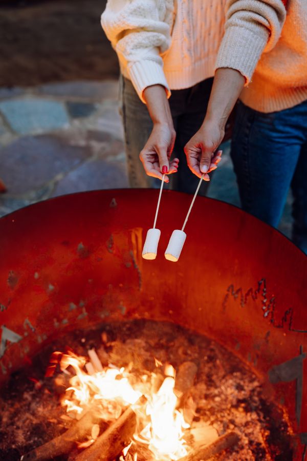 Night out with roasted marshmallows around bonfire. Cropped women hands holding sweet marshmallows on sticks near fire outdoors