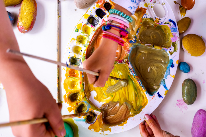 Children choosing colors in a paint palette with a brush enjoying art at home.