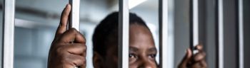 Young afro woman looking serious and desperate behind bars which may be prison bars or those of a security gate
