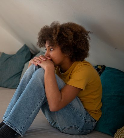 Teenage girl concerned sitting on sofa with her smartphone in background