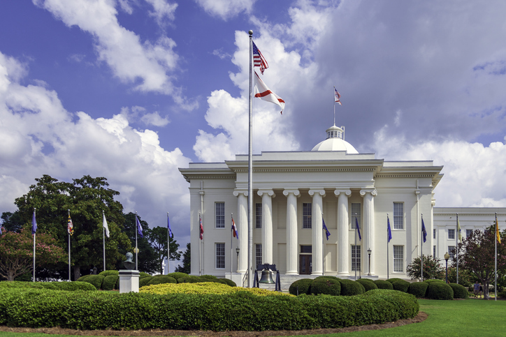 Montgomery Alabama State Capitol building with columns, steps, Dome, flags, a Liberty Bell replica, and beautiful landscaping