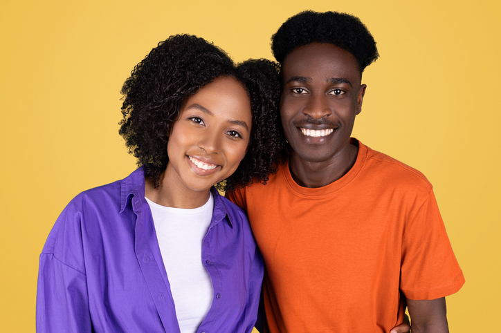 A portrait of a young, cheerful couple, with a woman in a purple blouse and a man in an orange shirt