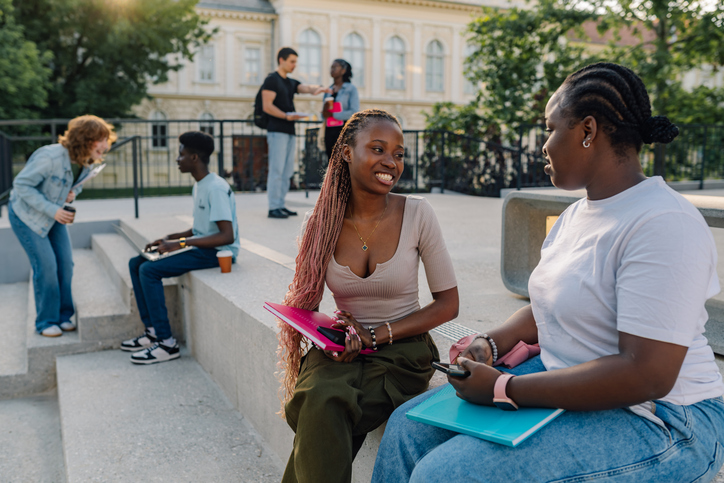 Happy interracial student girls on stairs at campus talking on break. Talking Black