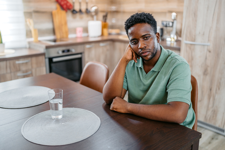 Sad Young Man Sitting At The Kitchen Table At Home
