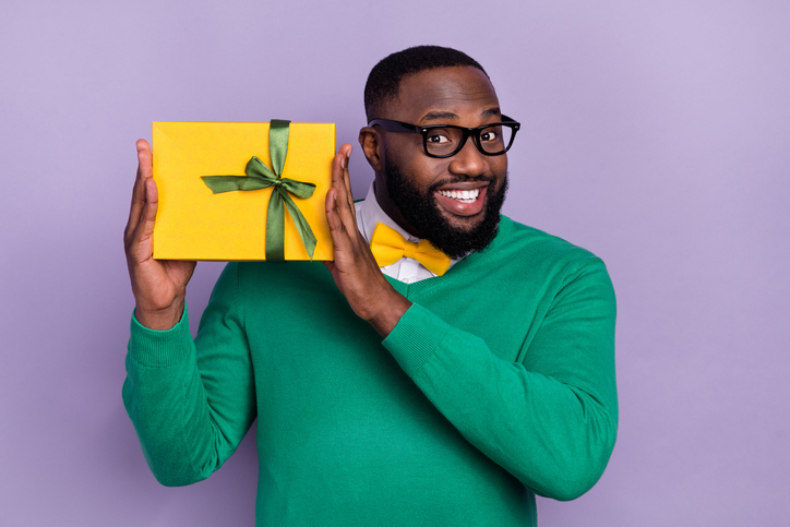 Portrait of positive nice man hold giftbox beaming smile look camera isolated on purple color background